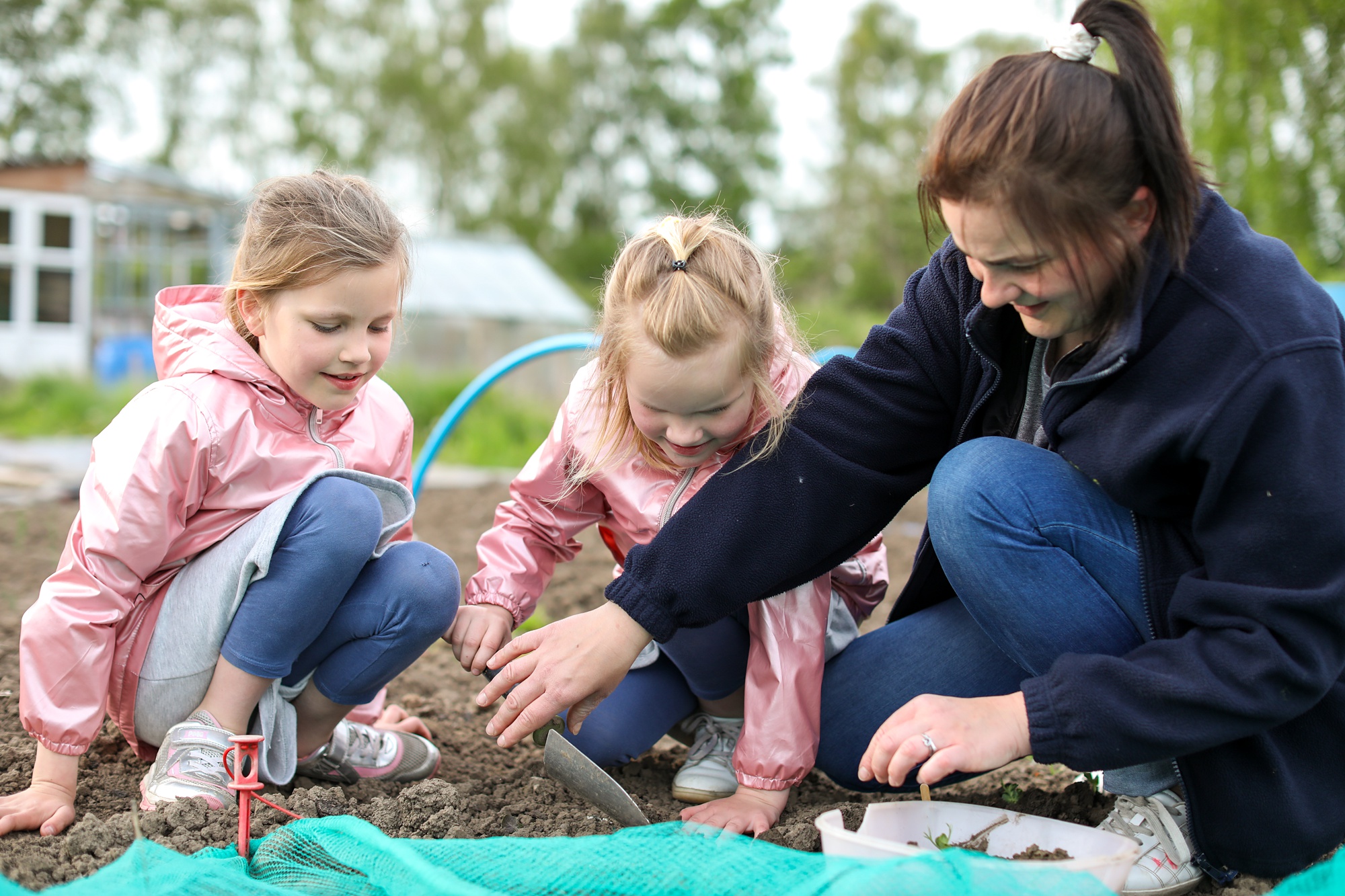 Family crouching down and playing in the soil in their garden